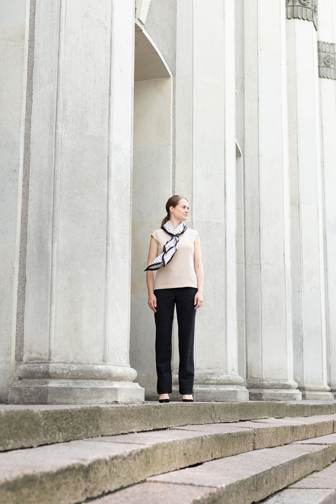 Designer is wearing a beige wool crepe blouse and black pants and silk scarf