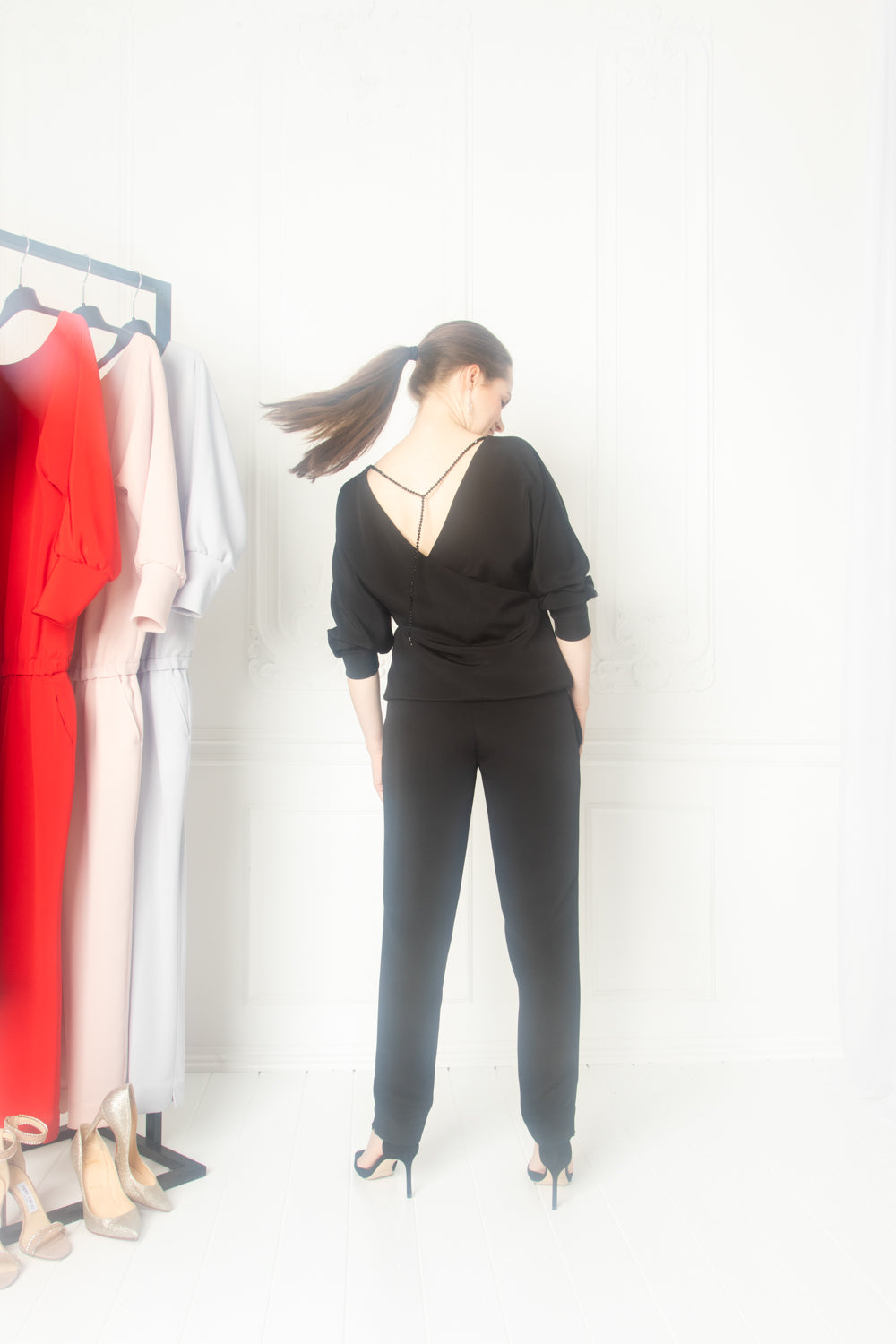 A brunette woman in wearing a black jumpsuit and a crystal back-chain as an accessory