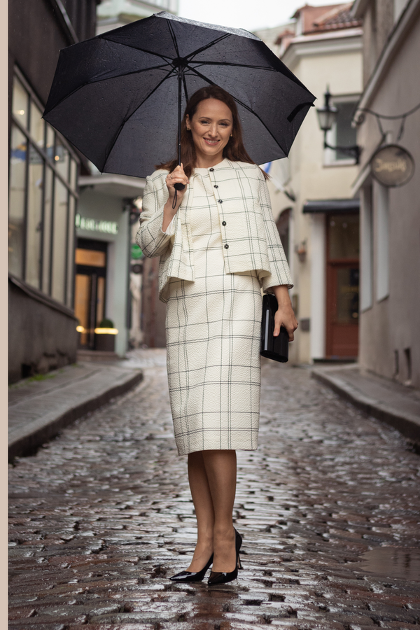 Woman in a checkered outfit holding an umbrella on a rainy street.