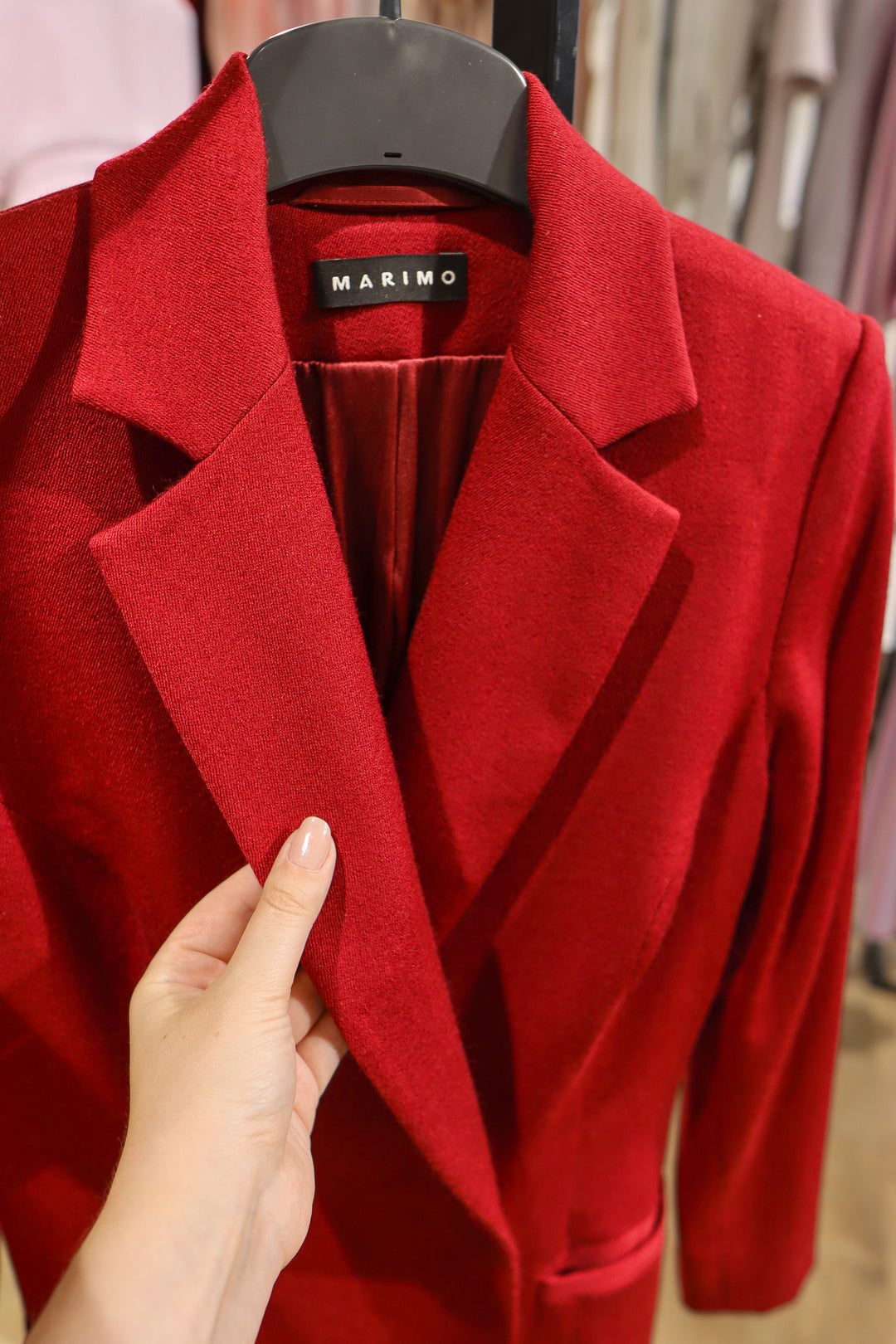 Red coat on a hanger with 'Marimo' label, held by a hand.