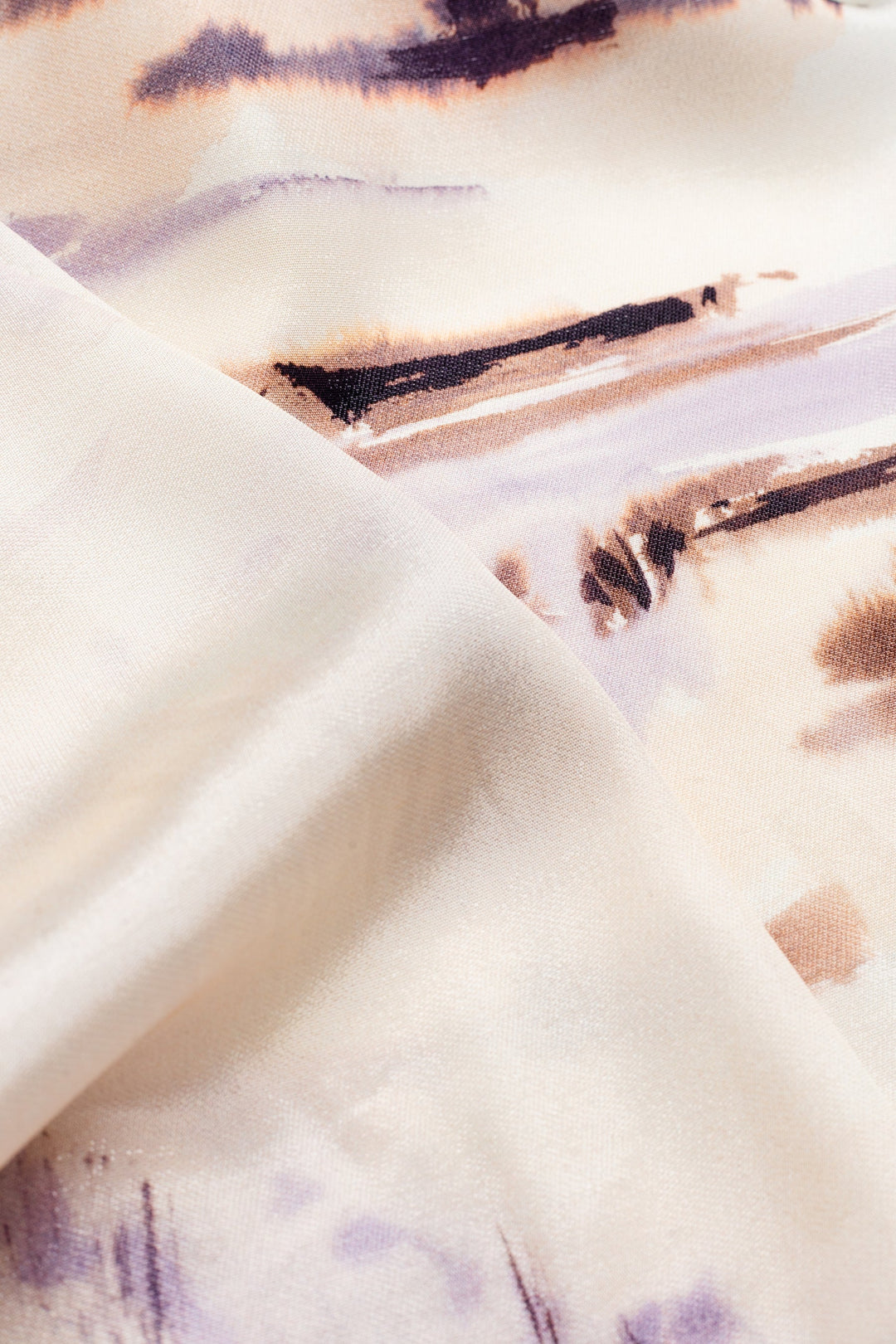 A close-up of draped fabric with an abstract watercolor-style print in cream, beige, light purple, and brown tones.