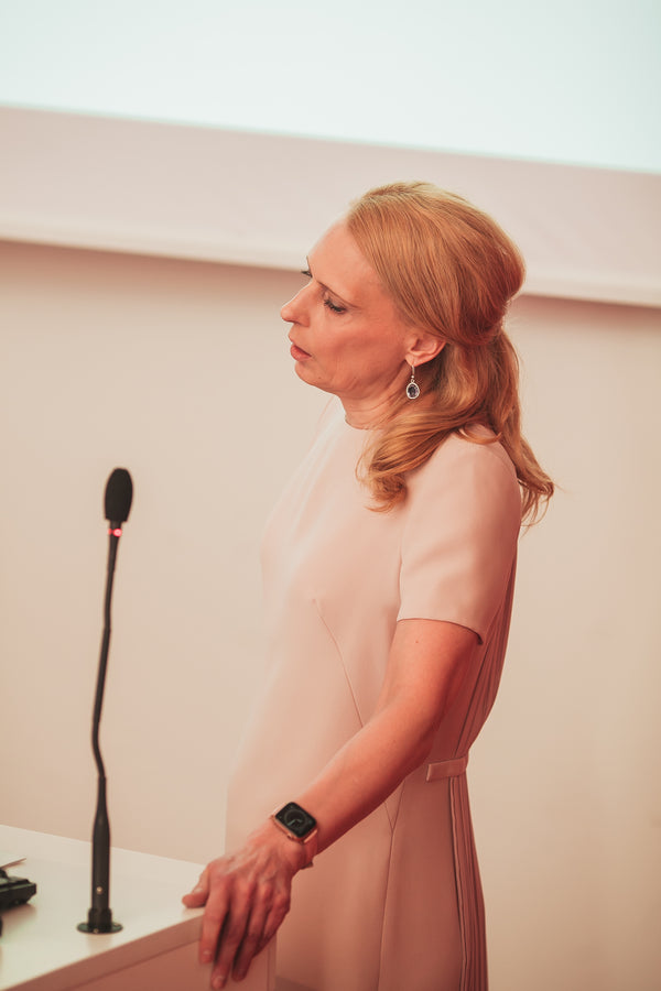 Woman in a pink dress standing in front of a microphone against a plain wall.
