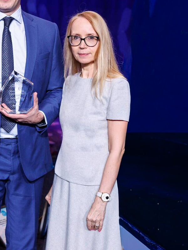 Woman in a light gray dress standing next to a man in a blue suit holding an award.