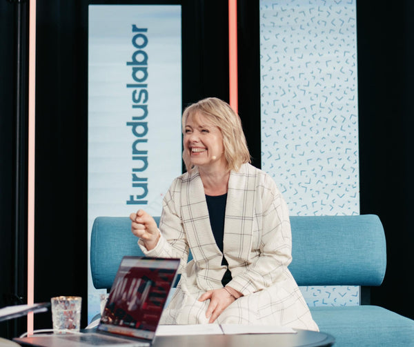 Woman in premium outfit sitting on a blue couch with a laptop, being interviewed