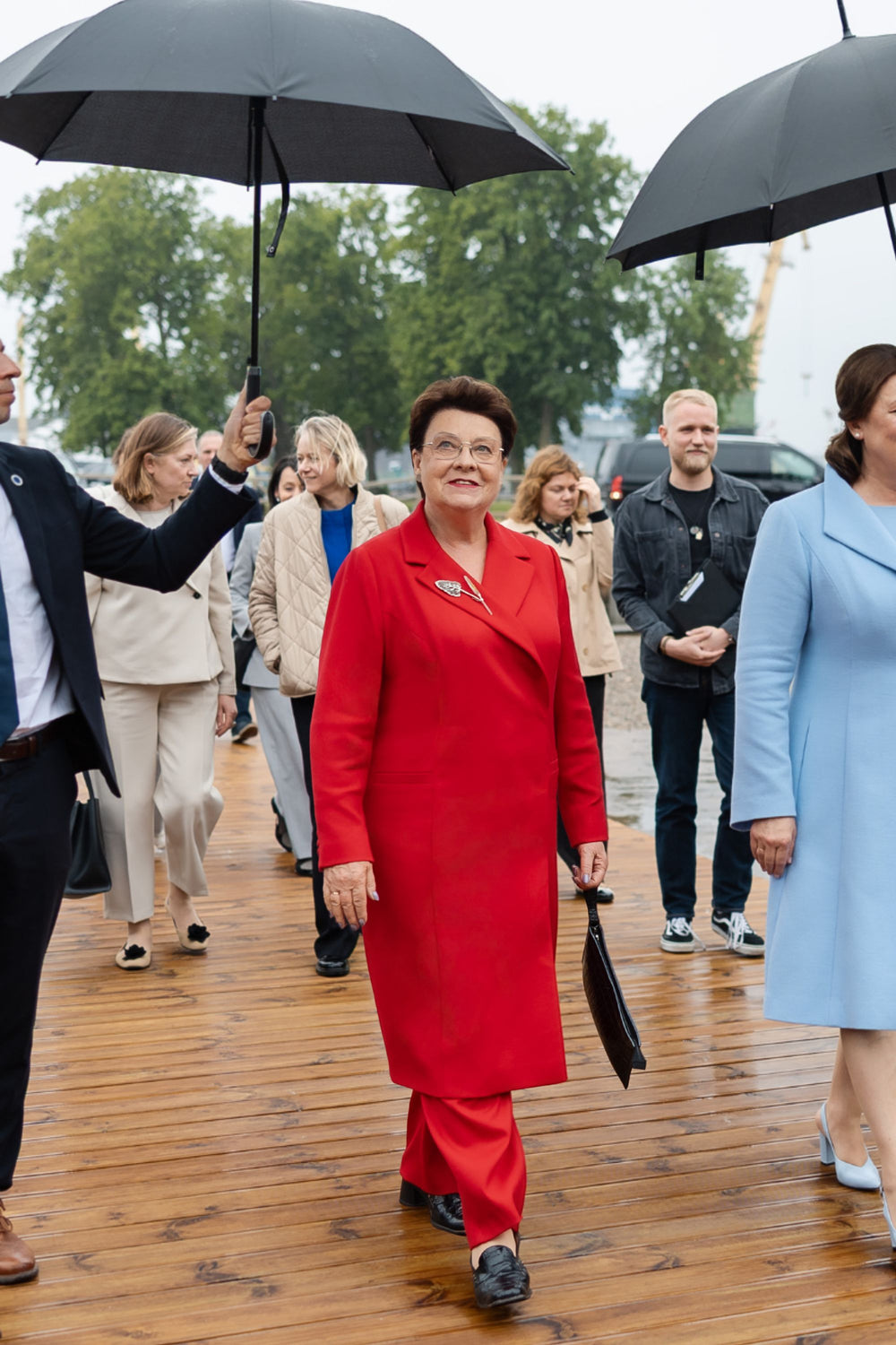 Important woman in a red suit walking outdoors with people holding umbrellas