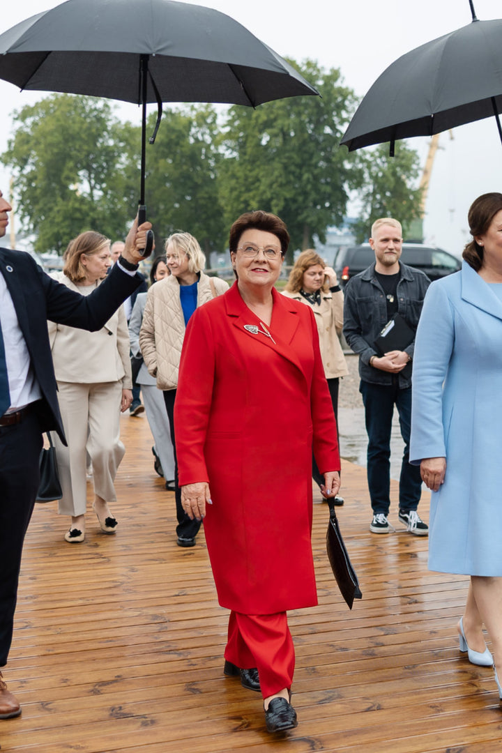 Important woman in a red suit walking outdoors with people holding umbrellas