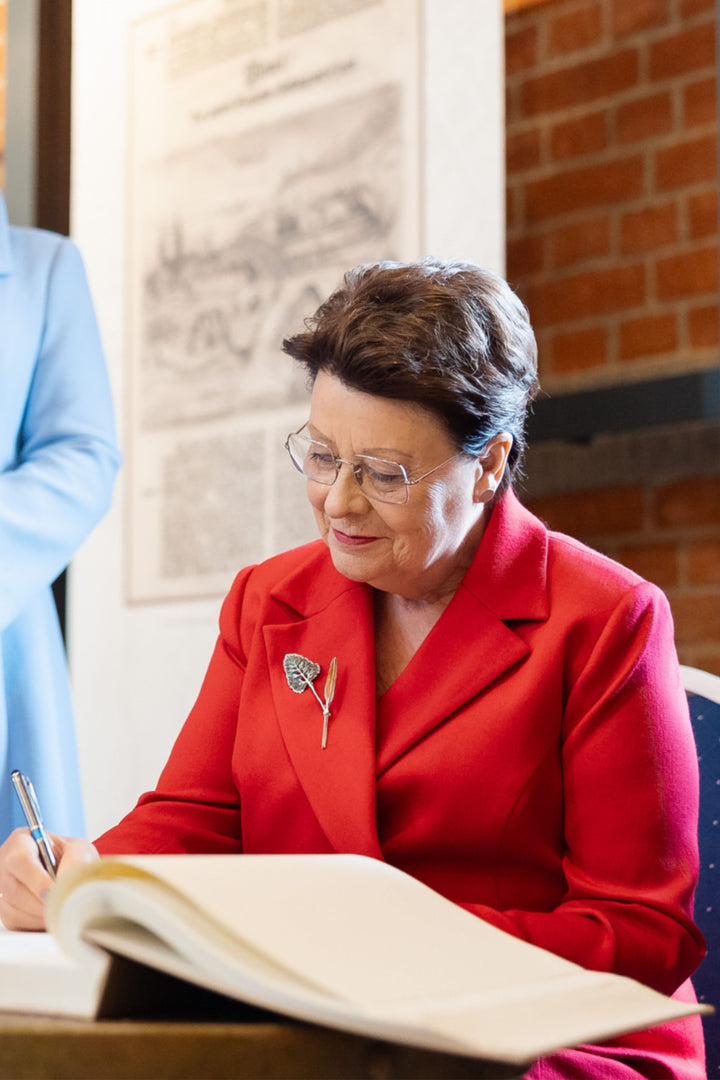 Woman in a red blazer signing a book with a brick wall in the background