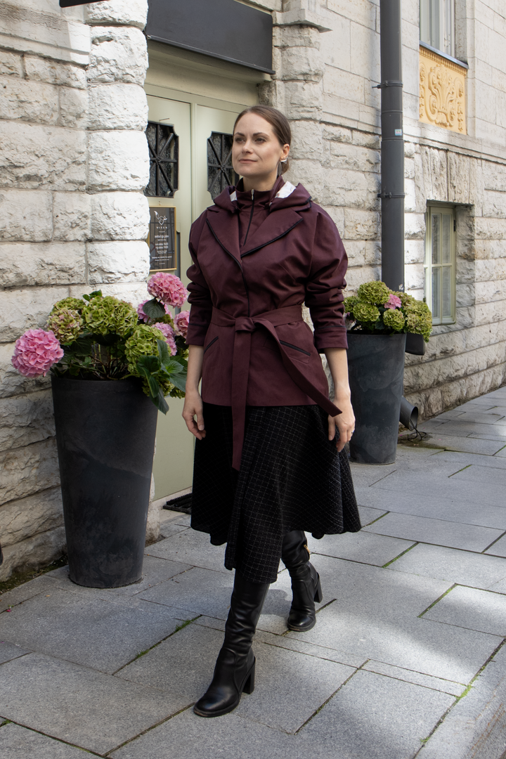 Woman wearing a muted burgundy luxury trench jacket on a city street.