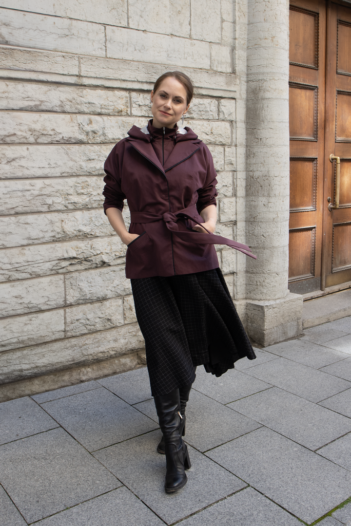 Woman wearing a minimalist muted burgundy trench coat with black dress on a city street.