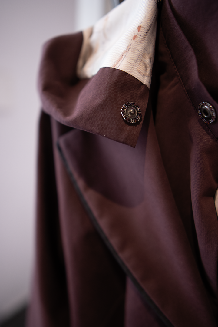 Removable hood detail of a muted burgundy trench jacket.