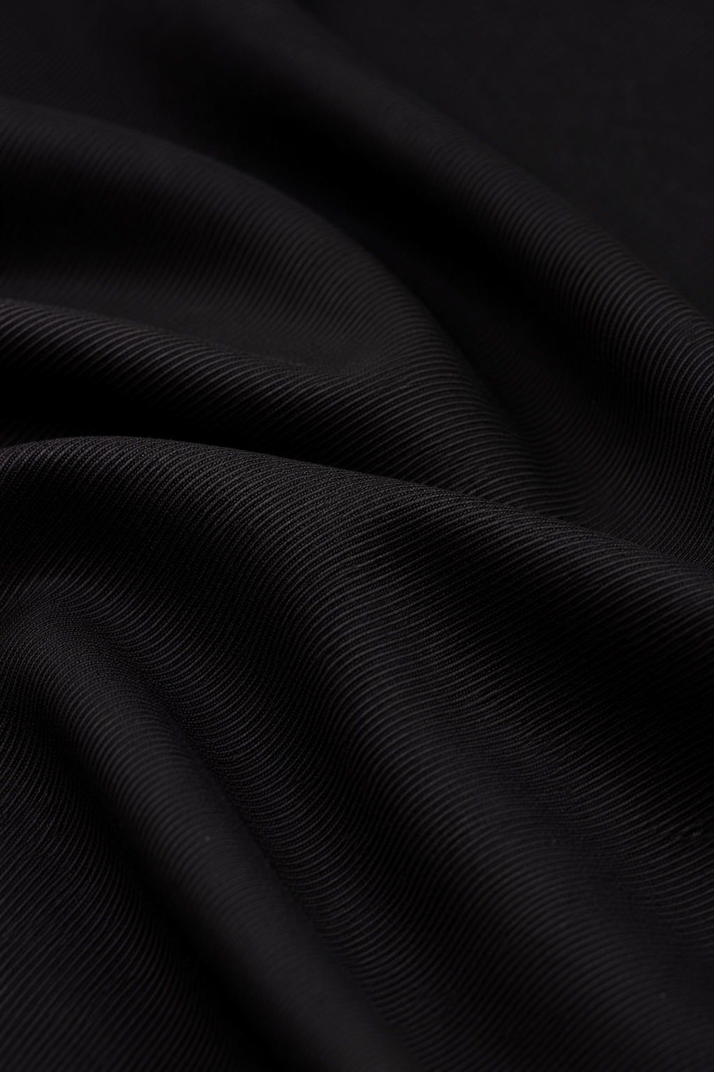 A close-up of draped black fabric with a fine ribbed texture, showing soft folds and shadows.