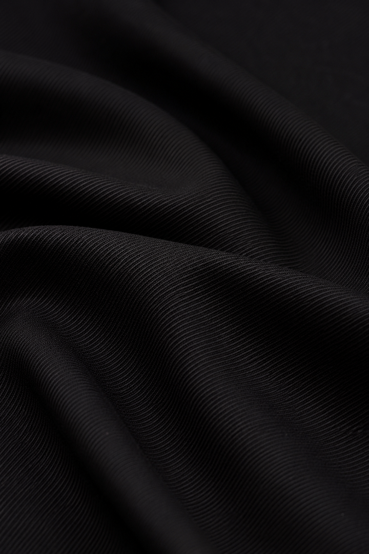 A close-up of draped black fabric with a fine ribbed texture, showing soft folds and shadows.